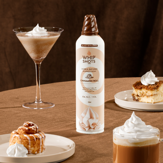 Bottle of Whip Shots Cinnamon Roll vodka with a cocktail and dessert on a wooden surface
