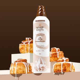 Whip Shots Cinnamon Roll flavored whipped cream bottle with cinnamon rolls on a brown background