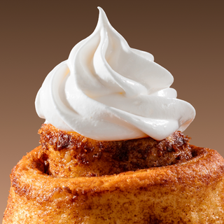 Cinnamon roll with white cream on a brown background