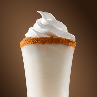 White cocktail with whipped cream and cookie crumb on a brown background
